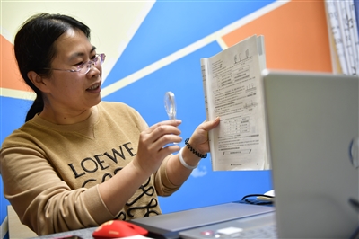 妻子王之玲拿著教材，在電腦前上初三物理課。